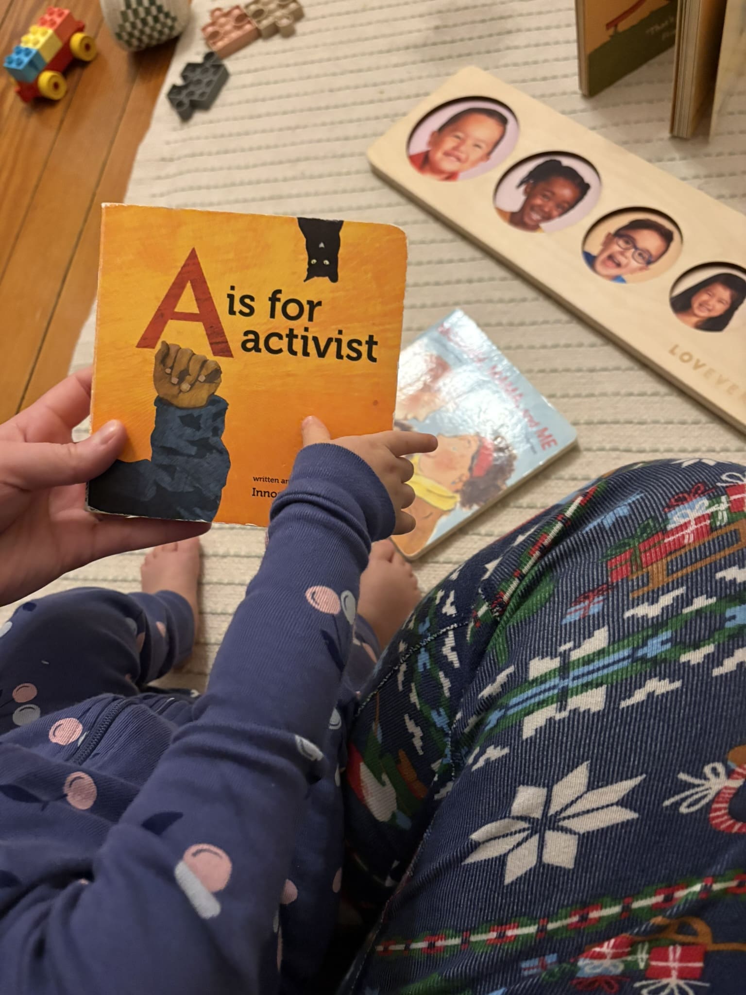 A parent holding their child in their lap, holding a copy of the children's book "A is for activist"