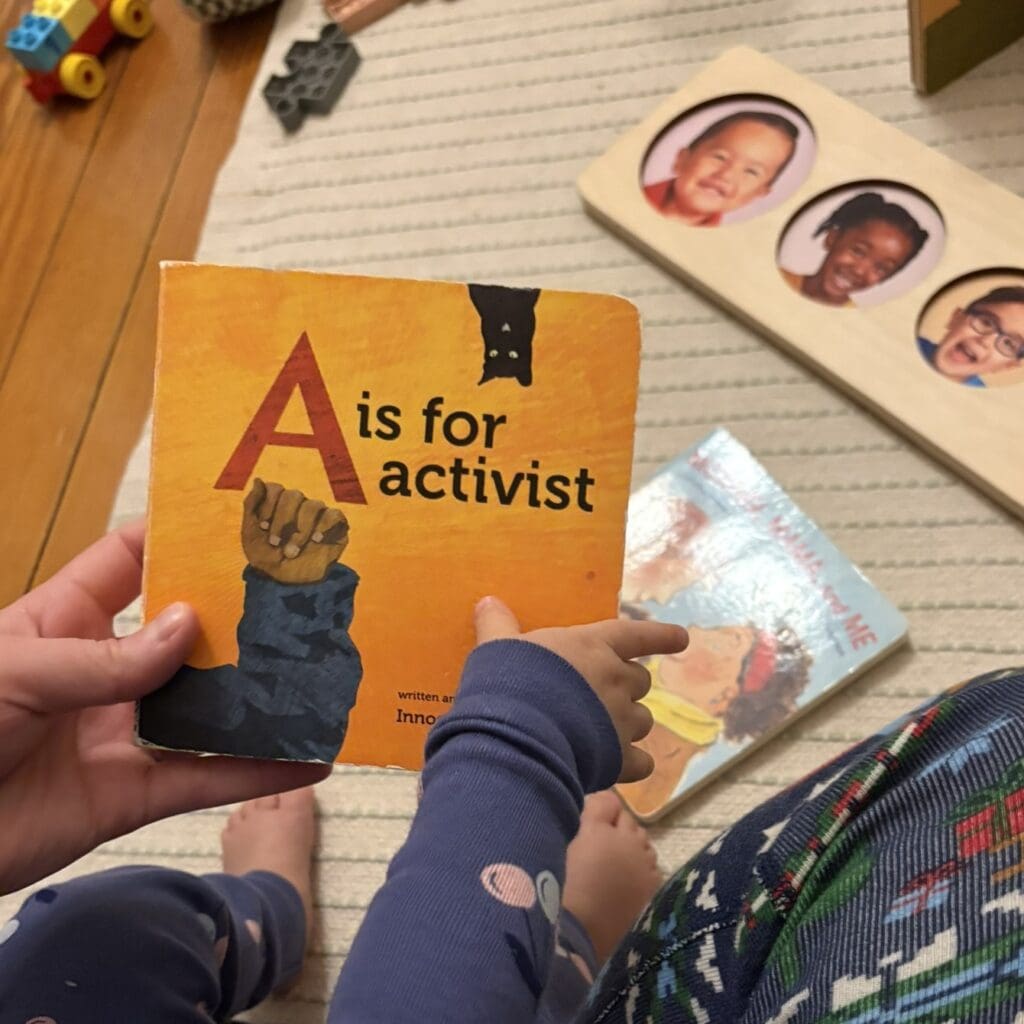 A parent holding their child in their lap, holding a copy of the children's book "A is for activist"